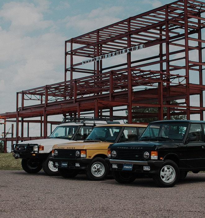 Three Land Rovers parked near steel frame building