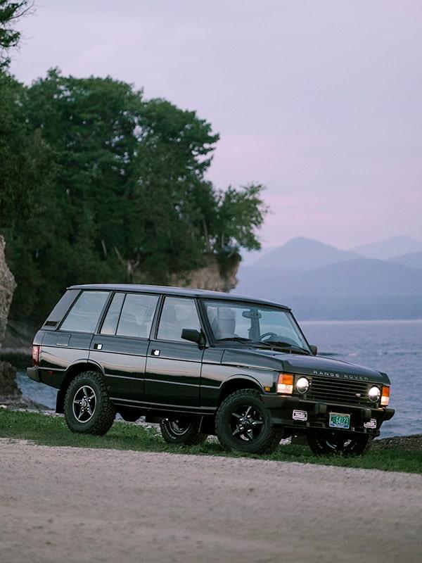 1995 Range Rover Classic parked by the water with mountains in the background